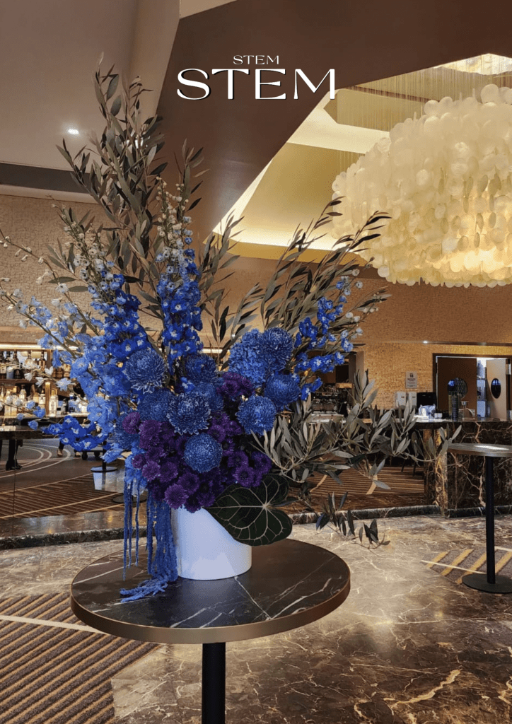 Floral arrangement of blue and purple flowers with olive foliage in a white vase at Bacchus Brisbane, The Ridges Hotel, styled by Stem Design – event florist Brisbane.