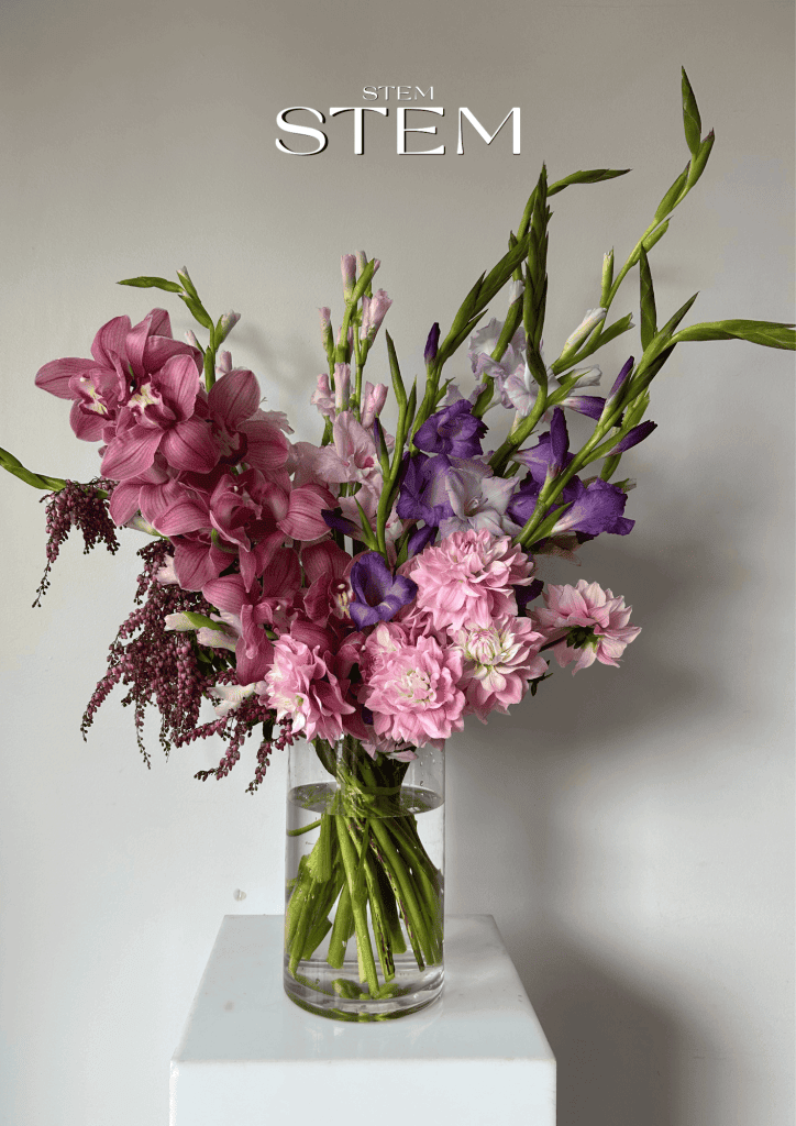 A vibrant floral arrangement of pink orchids, dahlias, and purple gladiolus in a glass vase, styled by Stem Design Brisbane.