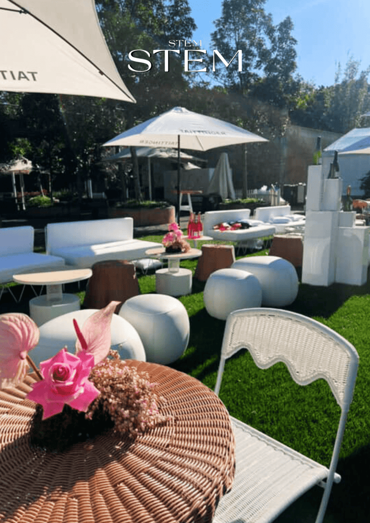 Outdoor event styled with white lounges, parasols, and wicker tables featuring pink roses, anthuriums, and baby’s breath by Stem Design in Brisbane.
