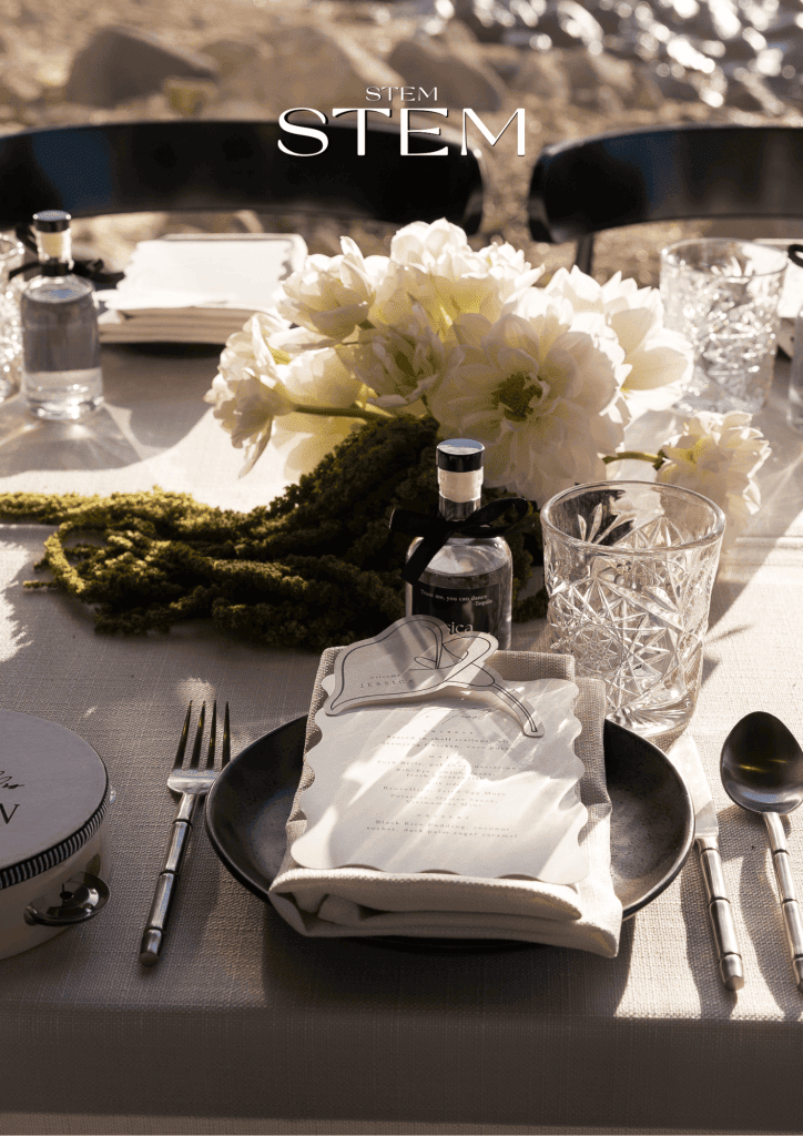 Low white wedding table arrangement with white dahlias and cascading green amaranthus styled at a coastal reception.