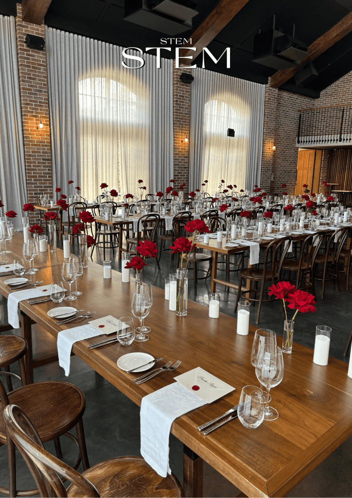 Long table wedding reception with minimalist red rose arrangements, candles, and timber tables styled by a wedding florist in Brisbane.