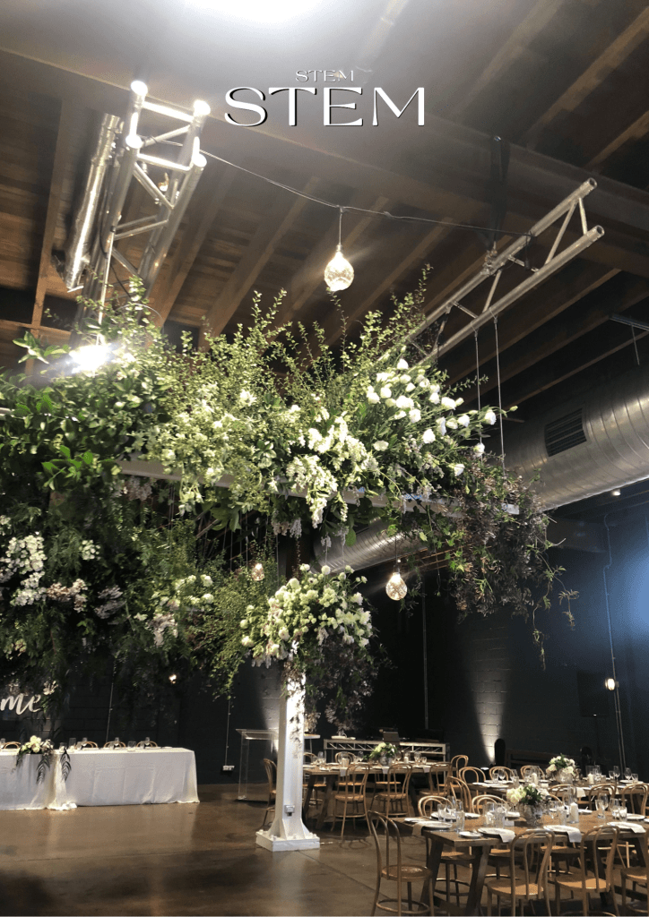 Suspended overhead floral installation with cascading greenery and white flowers above wedding reception tables in an industrial venue by Stem Design wedding florist Brisbane.