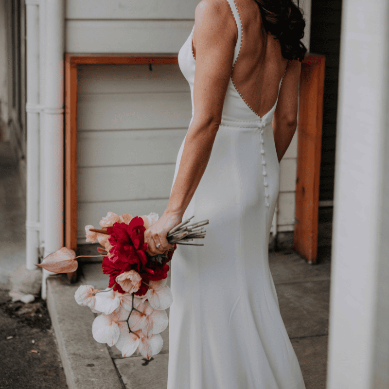 Bride holding red wedding flowers beside a window